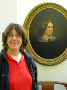 Stefani Koorey in front of painting of Carolyn Metcalf, Emma’s Principal